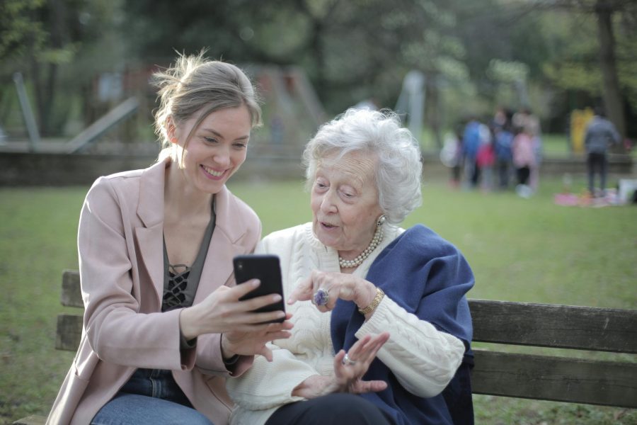 two women looking at a phone on a park bench